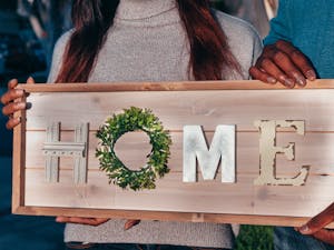 A couple holding a wooden sign spelling 'HOME' to celebrate their new residence.
